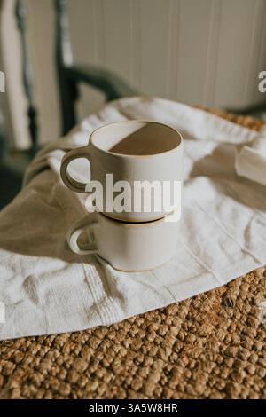 Deux tasses blanches sont assises sur un tissu blanc. Le tissu est sur une table en bois. Les tasses sont vides Banque D'Images