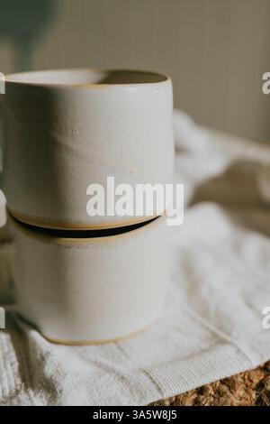 Deux tasses en céramique blanche reposent sur un chiffon blanc. Les tasses sont de forme et de taille identiques, et elles sont placées les unes à côté des autres. Concept de simplicité a Banque D'Images