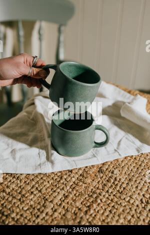 Deux tasses à café vertes sont assises sur une table avec un tissu blanc en dessous. Les tasses sont positionnées l'une sur l'autre et la table est couverte Banque D'Images
