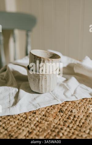 Deux tasses en céramique blanche reposent sur une nappe. Les tasses sont placées sur un tapis tissé. Concept de chaleur et de confort, comme les tasses et la nappe creat Banque D'Images