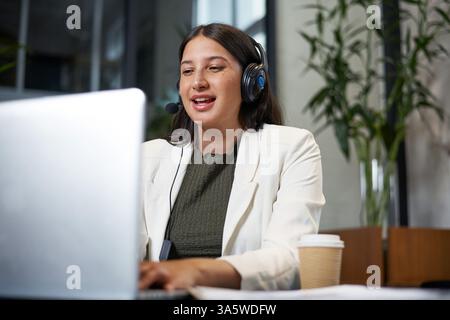 Femme professionnelle engagée dans une réunion virtuelle à l'aide d'un ordinateur portable et d'un casque dans le bureau Banque D'Images