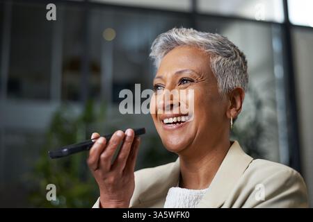 Femme d'affaires confiante communiquant avec l'appareil mobile dans l'espace de travail moderne Banque D'Images