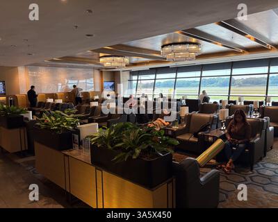 Intérieur d'un salon d'aéroport à Singapour avec des personnes se relaxant dans des chaises confortables avant leurs vols. De grandes fenêtres donnent sur l'aérodrome. Banque D'Images