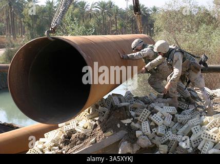13 nov. 2004 ; Lutafiyah, Irak ; Un marin et un marin de la 24e unité expéditionnaire des Marines mènent un tuyau dans une rivière à Lutafiyah, Irak, 13 novembre. Les tuyaux ont servi de base à un pont reconstruit qui a été gravement endommagé lors d'attaques répétées de militants anti-irakiens. La 24e MEU mène actuellement des opérations de sécurité et de stabilité dans la province de Babil, au nord du pays. Banque D'Images