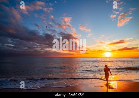 Un homme marche le long du bord de mer dans un beau coucher de soleil orange au bord de la mer Banque D'Images