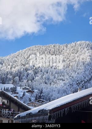 Scène hivernale idyllique du village enneigé de la Clusaz niché dans un paysage vallonné, Annecy, France. Les maisons en bois sont dispersées à travers la colline enneigée Banque D'Images