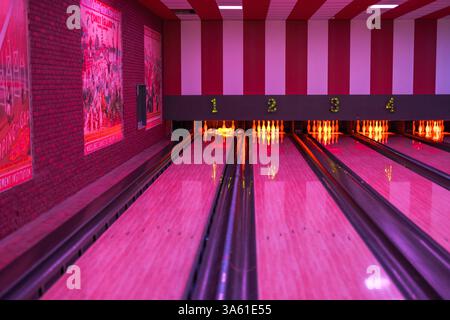Vue colorée de la piste de bowling vide avec des épingles incandescentes, un éclairage rouge et des affiches vintage sur le mur. Banque D'Images