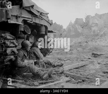 GEICH, ALLEMAGNE - 11 décembre 1944 - avec des obus allemands hurlant au-dessus de la tête, des fantassins américains cherchent refuge derrière un char. En arrière-plan peut être s. Banque D'Images