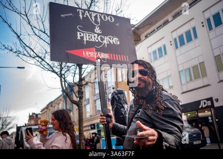 LONDRES - 4 MARS 2025 : une personne faisant la publicité de tatouage et de services de pièces sur Camden High Street, au nord-ouest de Londres Banque D'Images