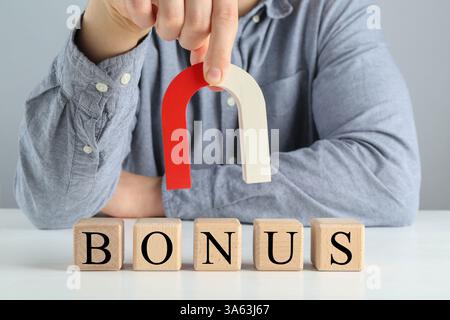 Femme tenant un aimant en fer à cheval sur des cubes en bois avec le mot Bonus sur la table Banque D'Images