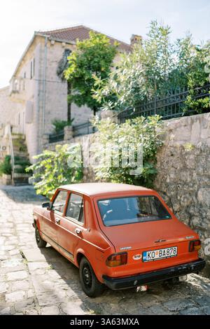 Monténégro, Kotor- 07 juillet 2024 : voiture vintage rouge Zastava Skala 101 se trouve près de la clôture en pierre d'une vieille maison Banque D'Images