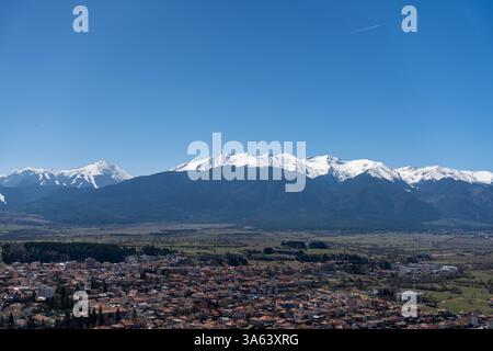 Vue panoramique sur la ville de Razlog nichée dans une vallée, avec les imposantes montagnes Pirin s'élevant en arrière-plan sous un ciel bleu immaculé Banque D'Images