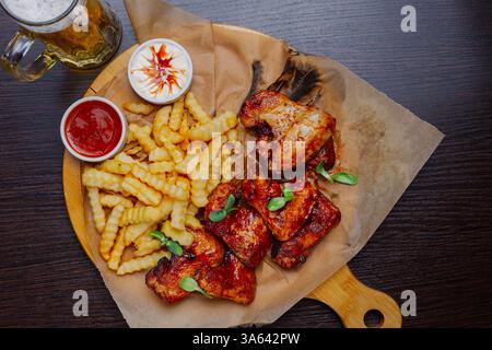 Ailes frites appétissantes avec sauce aux frites et bière sur une planche de bois. vue de dessus Banque D'Images