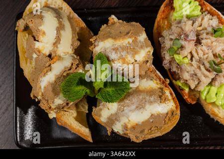 Trois types de bruschetta sur la table sur une assiette noire belle servir dans un restaurant. collation classique. gros plan de bruschetta avec pâté et beurre Banque D'Images