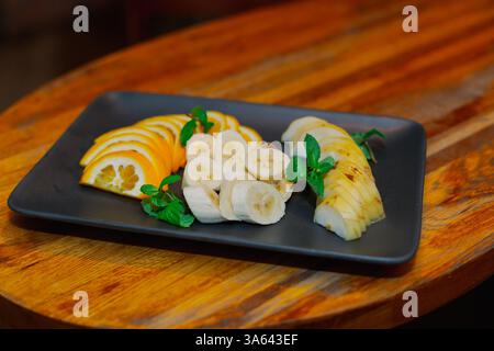 Des fruits magnifiquement hachés sur une assiette noire décorée de menthe, tout cela se tient sur une table en bois dans un restaurant Banque D'Images