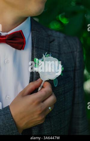 Un jeune marié est très heureux le jour de son mariage et ajuste une belle boutonnière sur sa veste avant la cérémonie de mariage Banque D'Images