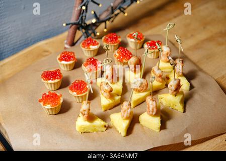 Assortiment d'aliments pour les doigts comprenant des crevettes sur des brochettes d'ananas et des tartelettes recouvertes de caviar rouge, organisées pour un événement festif. Banque D'Images