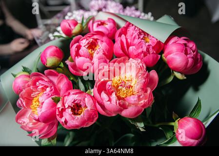 Bouquet luxuriant de pivoines roses vibrantes enveloppées dans du papier vert, parfait pour les cadeaux romantiques, les mariages ou les célébrations du printemps. Banque D'Images