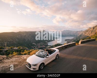 Monténégro, Kotor - 13 juillet 2024 : mariés et mariés conduisent dans un cabriolet le long d'une route au-dessus de la baie de Kotor. Monténégro. Drone Banque D'Images
