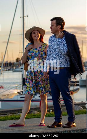 un couple élégant profite d'une promenade près d'une marina pittoresque pendant le coucher du soleil, portant des vêtements d'été élégants et vibrants, l'atmosphère sereine et bac pittoresque Banque D'Images