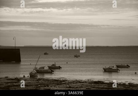 Cancale (Bretagne) au coucher du soleil. Amarrage des voiliers et vue sur la silhouette rêveuse du Mont Saint Michel à l'horizon. Photo sépia. Banque D'Images
