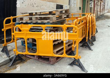 Barrières de construction en plastique orange vif empilées près de palettes en bois dans une rue urbaine. EQUIPEMENT de sécurité pour travaux routiers, construction Banque D'Images