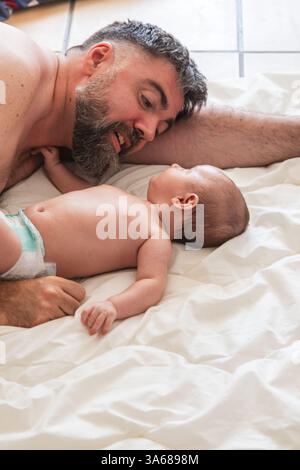 Père allongé sur le lit jouant avec son fils bébé portant une couche Banque D'Images