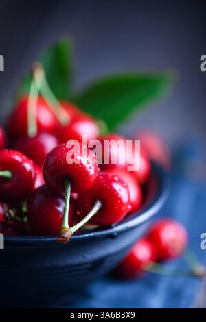 Cerises mûres sur bol noir gros plan. Photographie culinaire Banque D'Images