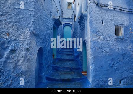 Marches bleues et murs menant à une porte en bois bleu clair dans la rue bleue de la médina de la vieille ville, Chefchaouen, Maroc Banque D'Images