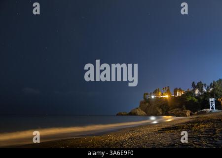 Vue panoramique de nuit d'une plage de Nerja, à Malaga, Espagne. Les lumières des maisons de la côte sont reflétées dans l'eau de mer et il y a des étoiles en t Banque D'Images