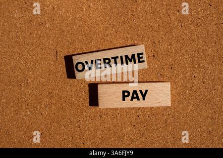 Message de paie d'heures supplémentaires écrit sur des blocs de bois sur fond brun. Symbole conceptuel de rémunération des heures supplémentaires. Copier l'espace. Banque D'Images
