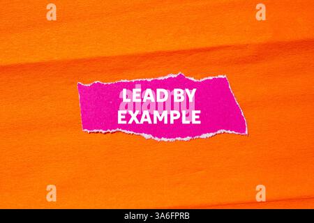 Dirigez par l'exemple message écrit sur papier rose déchiré déchiré sur fond orange. Symbole de la direction conceptuelle par exemple. Copier l'espace. Banque D'Images