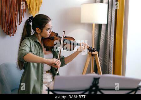 Jeune femme jouant du violon à la maison par partition, axée sur l'apprentissage de la musique Banque D'Images