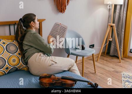 Femme concentrée pratiquant le rythme de violon avec des conseils de partitions Banque D'Images