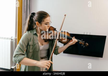Jeune femme jouant du violon à la maison par partition, axée sur l'apprentissage de la musique Banque D'Images
