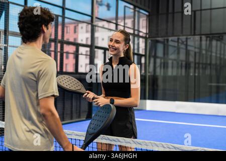 Jeune femme et homme jouant au padel, souriant et tenant des raquettes sur le court Banque D'Images