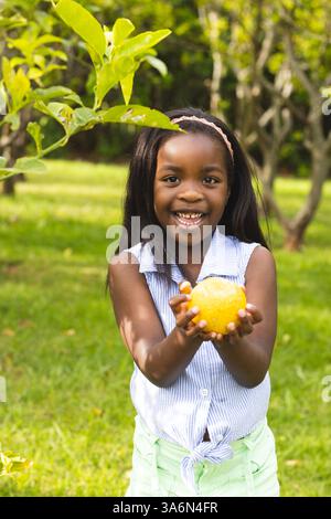 Fille souriante tenant du citron dans le jardin, profitant de la journée ensoleillée à l'extérieur Banque D'Images
