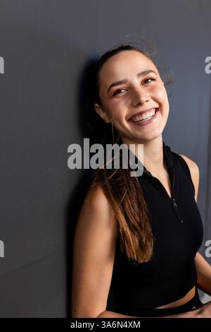 Jeune femme souriante en vêtements athlétiques appuyée contre le mur après le padel tennis Banque D'Images