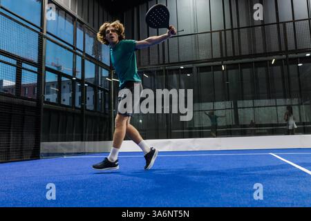 Jeune homme jouant au padel sur un court intérieur, balançant énergiquement la raquette Banque D'Images