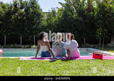 Diverses amies féminines se relaxant au bord de la piscine, profitant d'une journée ensoleillée et discutant sur des serviettes colorées Banque D'Images