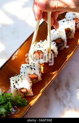 plateau de saumon sushi maki et une main tenant des baguettes ramenant un Banque D'Images