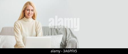 Jeune femme travaillant sur ordinateur portable à la maison tout en étant assis sur un canapé confortable pendant la journée Banque D'Images