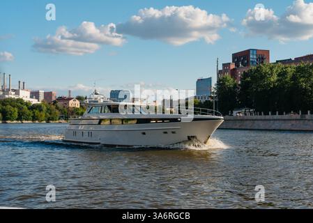 Moscou Russie - juillet 30 2023 - Un yacht blanc élégant navigue le long d'une rivière urbaine avec des bâtiments, des arbres et des cheminées industrielles en arrière-plan Banque D'Images