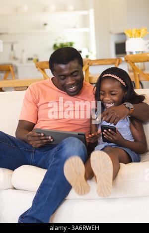 Père et fille riant ensemble tout en utilisant des tablettes sur le canapé du salon Banque D'Images