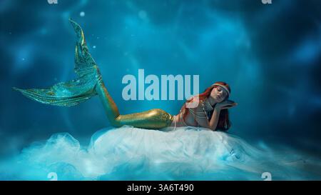 Femme rêveuse comme sirène reposant sur un tissu flottant, son expression douce se mêlant au mouvement fluide du monde sous-marin. Banque D'Images