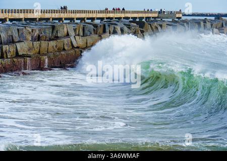 De puissantes vagues océaniques s'écrasent contre le rivage rocheux près de Cabrillo Beach Pier, avec pêcheurs et visiteurs silhouettes sur fond de cercle Banque D'Images