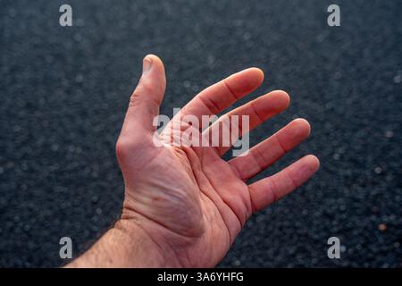 Main blanche de l'homme adulte sur fond noir de sable de plage en contraste élevé Banque D'Images
