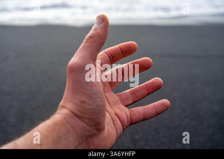 Main blanche de l'homme adulte sur fond noir de sable de plage en contraste élevé Banque D'Images