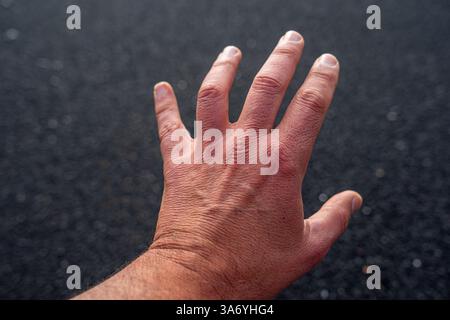 Main blanche de l'homme adulte sur fond noir de sable de plage en contraste élevé Banque D'Images
