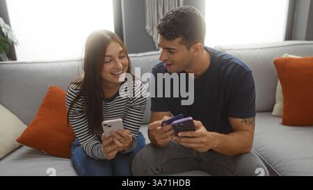 Homme et femme assis ensemble sur un canapé dans un salon souriant et regardant leurs smartphones. Banque D'Images